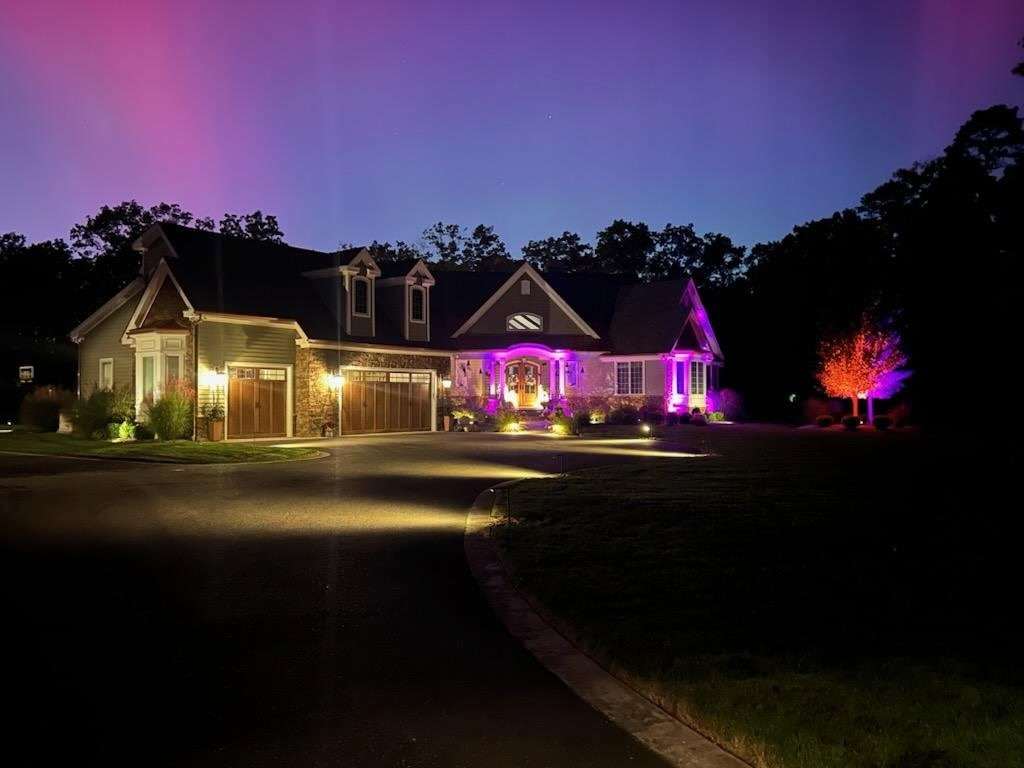 Northern lights above a home lit with Wetlawn uplighting